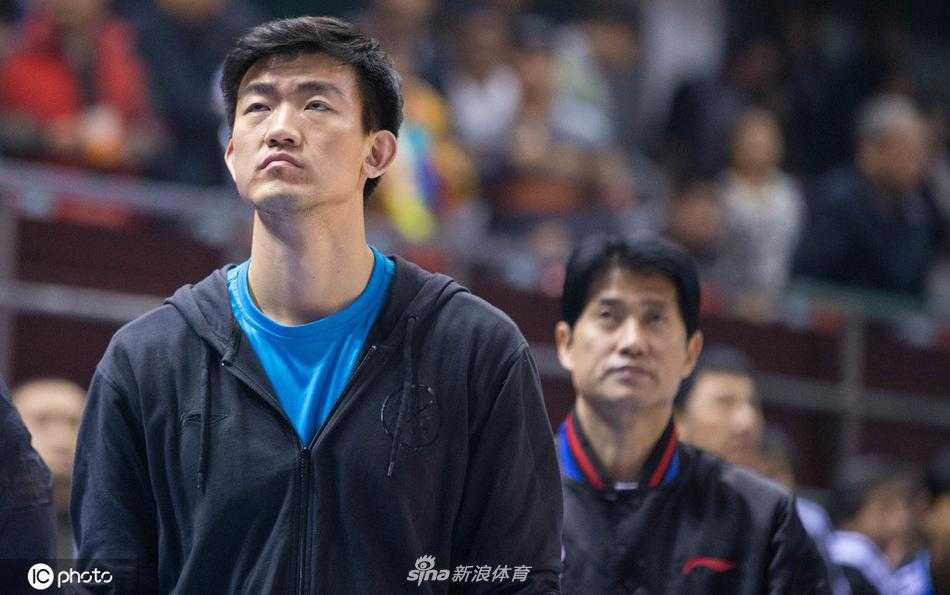 王博在场边双手插兜面带微笑注视着比赛，神情放松中带着自信，身后的广厦球迷挥舞着助威旗帜