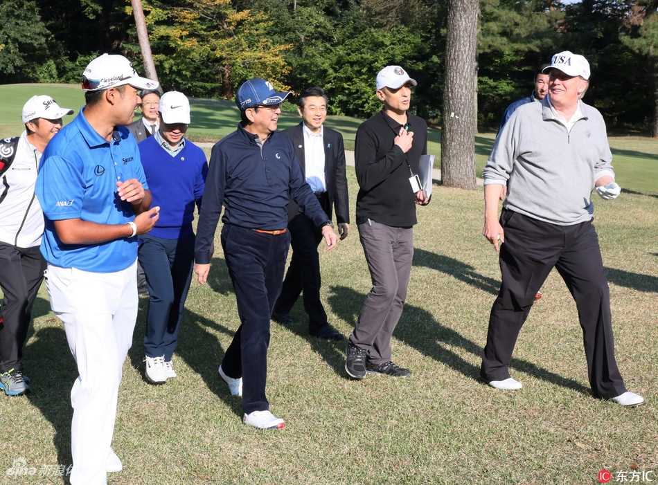 日本埼玉县霞关乡村俱乐部，日本首相安倍晋三与美国时任总统特朗普面带笑容，伸出拳头互相撞击致意，背景是绿草如茵的高尔夫球场。
